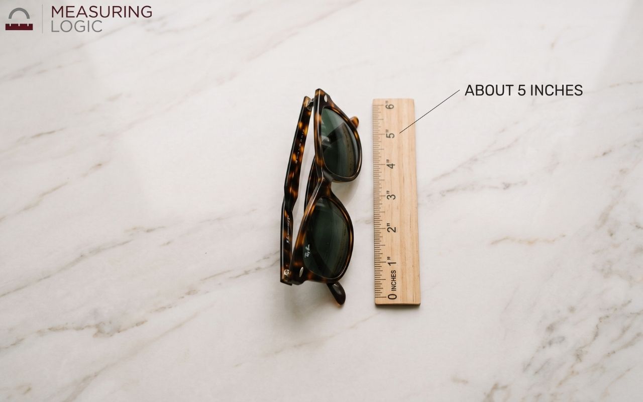 Folded sunglasses next to a small ruler on a marble surface