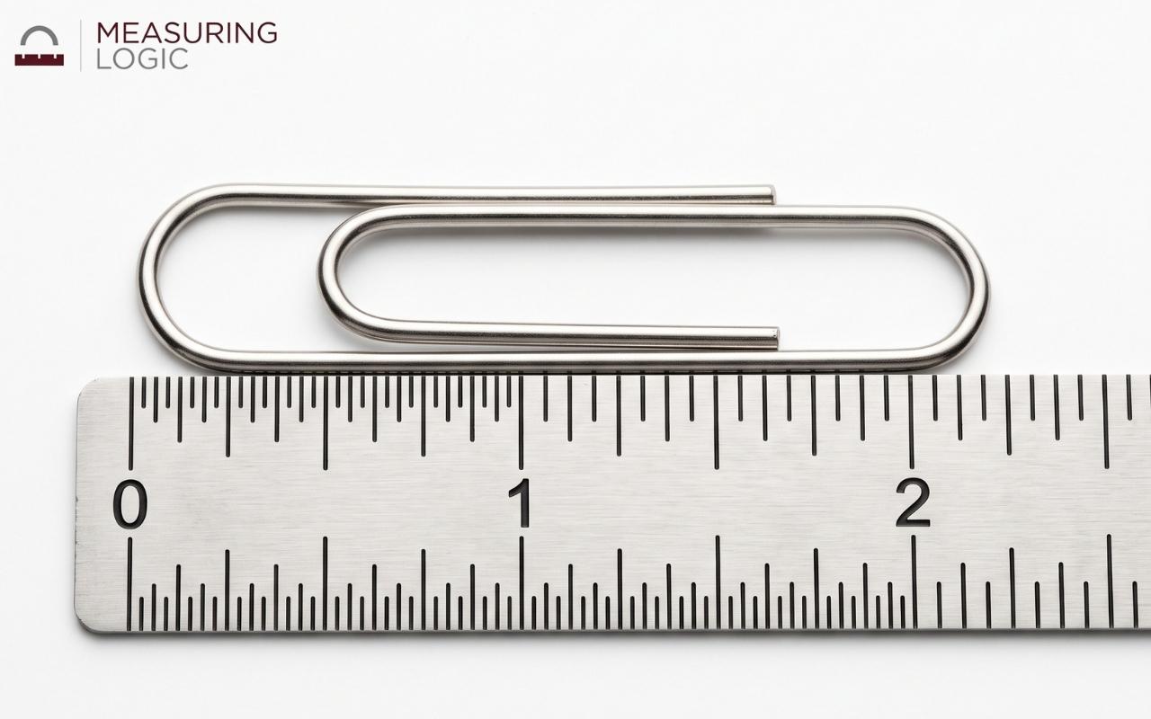 A jumbo paperclip lying flat next to a ruler showing its 2-inch length.