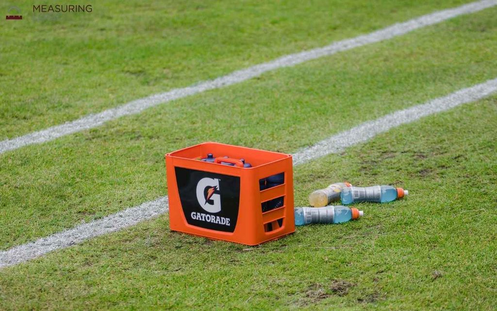 An orange Gatorade crate sitting on a green sports field next to painted white boundary lines.