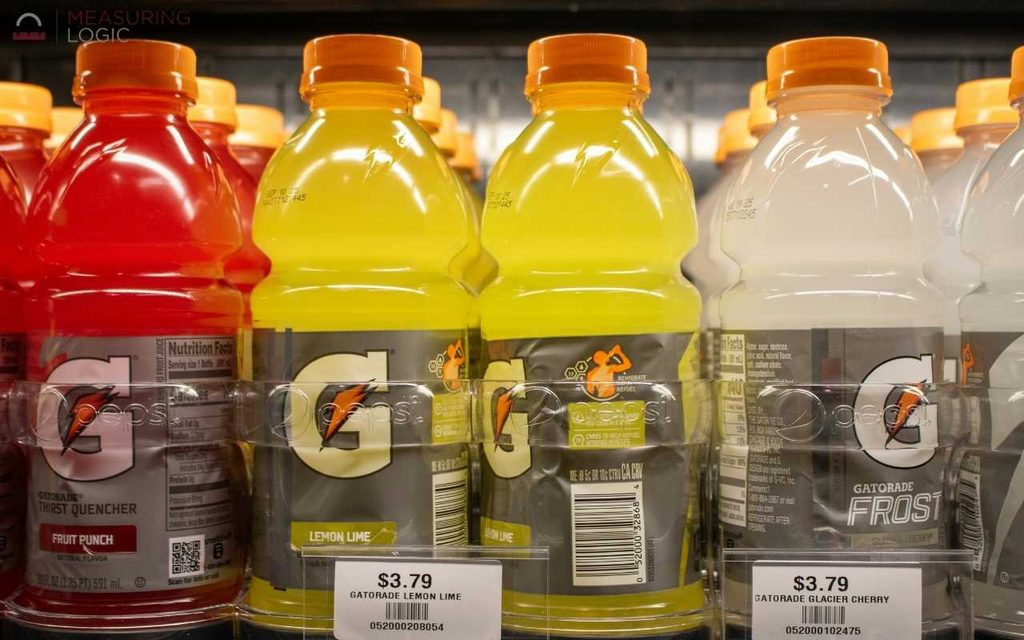 Assorted flavors of 20 fl oz Gatorade bottles lined up on a grocery refrigerator shelf behind price tags.