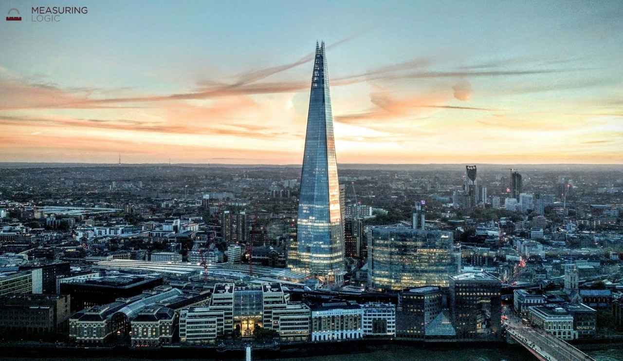 A wide aerial view of the London skyline at sunset featuring The Shard, a famous skyscraper that stands approximately 1000 feet tall.