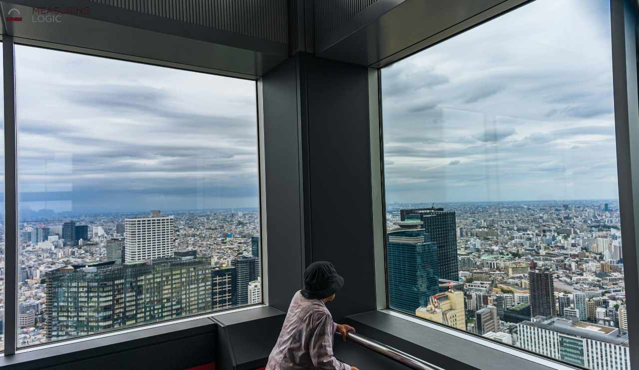 A person looking out from a high-rise glass observation deck over a sprawling cityscape