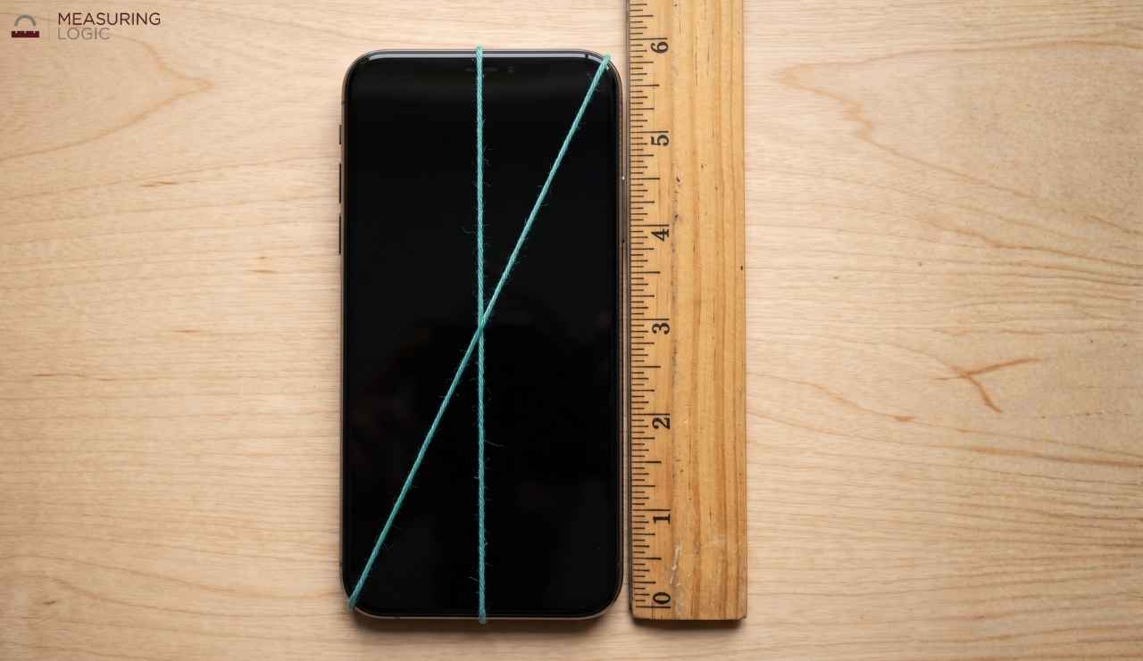 Clean top-down photo of a smartphone with a blank screen on a desk. A thin teal string runs corner to corner diagonally across the screen, and a second thin teal string runs vertically along the phone's full height.